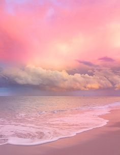 the sky is pink and purple over the ocean with waves coming in to shore on a cloudy day