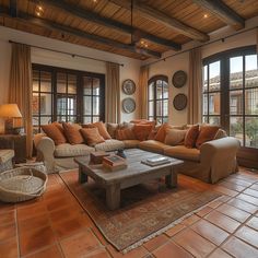 a living room filled with lots of furniture next to two large windows on top of a wooden ceiling