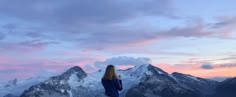 a woman standing on top of a snow covered mountain looking at the sky with mountains in the background