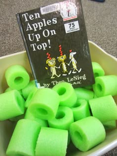 there are many green objects in the bowl on the floor next to a book that says ten apples up on top