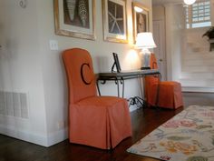 two orange chairs are sitting in front of a wall with pictures on it and a rug