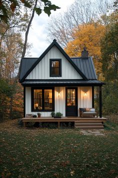 a small white house in the woods with black shingles and a porch that has steps leading up to it