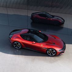 two red sports cars parked next to each other in front of a metal wall and floor