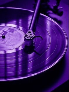 a record player's turntable is shown in this purple photo, with the music playing on it