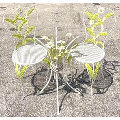 three metal chairs and two tables with flowers in them on the ground near each other