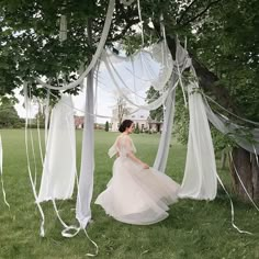 a woman in a wedding dress standing under a tree with white drapes hanging from it's branches