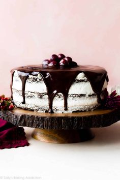 a cake with chocolate icing and cherries sitting on top of a wooden platter