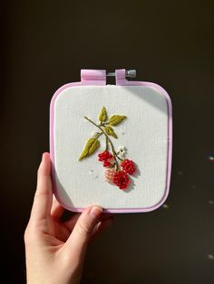 a hand holding a small embroidered object with flowers on it's front and side