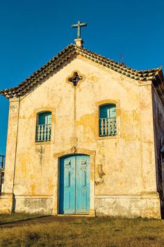 an old church with a cross on the roof and blue doors in front of it