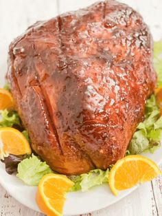 a large piece of meat sitting on top of a white plate next to oranges and lettuce