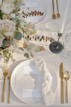 the table is set with white and gold place settings, silverware, and flowers