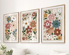 three floral paintings hang on the wall next to a white couch and vase with flowers in it