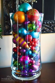 a glass vase filled with colorful ornaments on top of a wooden table next to a mirror