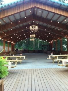 an outdoor pavilion with lights strung from the ceiling and benches on the ground in front of it