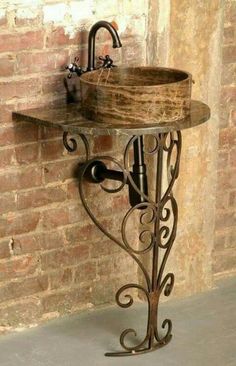 a bathroom sink sitting on top of a metal stand next to a brick wall with a faucet