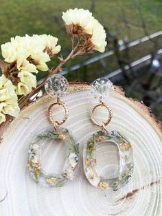 two pairs of earrings sitting on top of a piece of wood next to some flowers