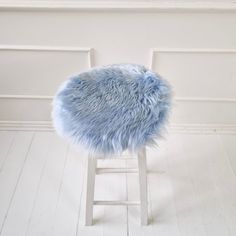 a stool with a blue fur on it in front of a white wall and floor