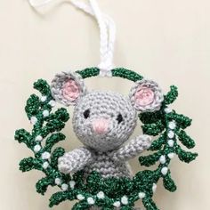 a crocheted mouse ornament hanging from a white string on a wall