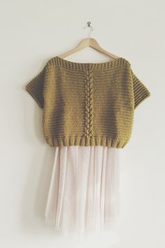 a knitted sweater hanging on a wall next to a hanger with a white dress underneath it