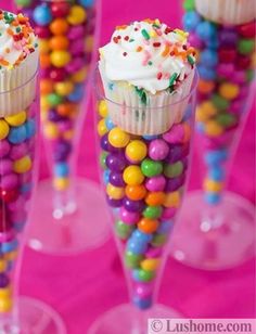 cupcakes with sprinkles and candy are in wine glasses on a pink table