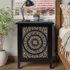 a black and gold patterned cabinet next to a bed with a plant on the side