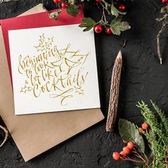 a christmas card with gold lettering on it next to holly branches and other holiday decorations