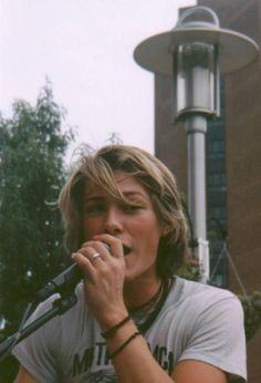 a young man singing into a microphone in front of a street light and lamp post