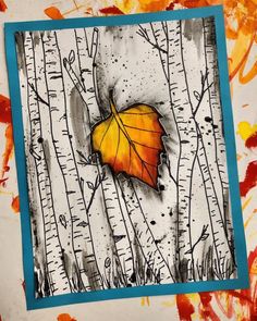 an orange leaf sitting on top of a white and blue paper with trees in the background