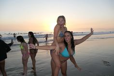 two women in bikinis are on the beach with their arms around each other and one is carrying another woman