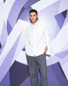 a man standing in front of a purple and white wall with his hands in his pockets