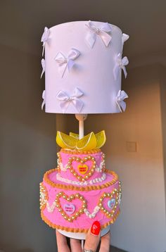 a pink cake with yellow bow on top being held by a woman's hand