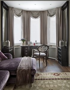 a living room with a couch, chair and desk in front of two large windows