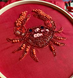 a red crab is embroidered on a pink background with bead work in the middle