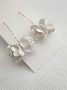 two white flowers are sitting on top of a piece of paper next to a pair of earrings