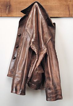 a brown leather jacket hanging on a wooden coat rack with two coats attached to it