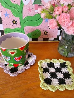 a crocheted coaster next to a cup of tea on a table with pink flowers