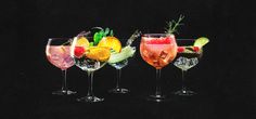 three glasses filled with different types of drinks on top of a black surface, one has an orange slice and the other has a green garnish