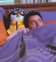 a man laying in bed with a stuffed penguin