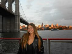 a woman standing in front of a bridge with the city skyline in the back ground