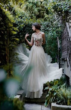 a woman in a white dress is walking through some bushes and trees with her hair blowing in the wind