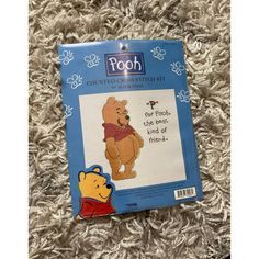 the winnie the pooh cross stitch kit is laying on top of a carpet with it's tag