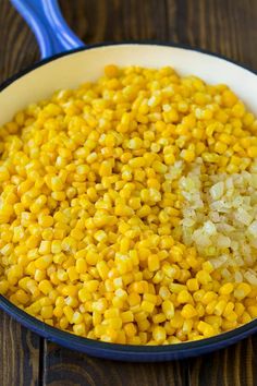 corn in a bowl with a blue spoon on the side and brown wooden table top