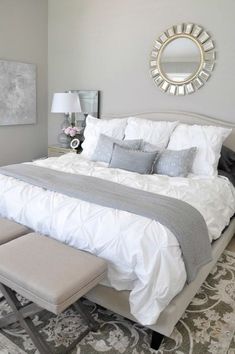 a bed with white sheets and pillows in a bedroom next to a mirror on the wall