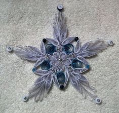 a snowflake made out of paper and beads on a white blanket with buttons