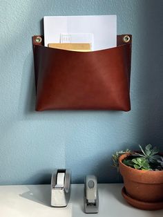 a brown leather wallet hanging on a blue wall next to a phone and plant in a pot