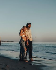 a man and woman standing on the beach next to each other with their arms around one another