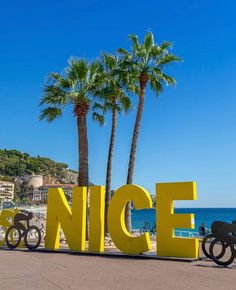 a large yellow sign that says nice next to the beach with palm trees in front of it