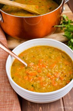 a bowl of soup with carrots and parsley next to a pot of stew