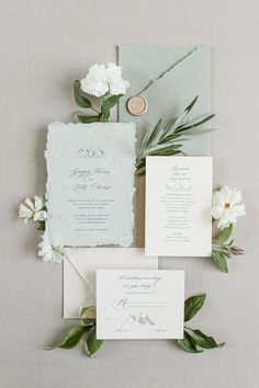 the wedding stationery is laid out with white flowers and greenery