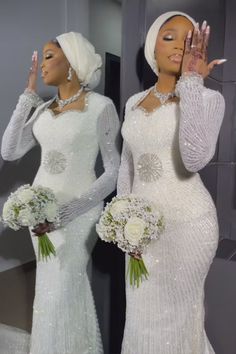 two women in white dresses standing next to each other and one is holding her hand up